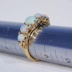 "This Victorian ring was handcrafted in England around 1900. It's a glimmery little stunner featuring five round cabochon opals patterned with 10 rose cut diamonds. The largest opal can be found at the center of the ring face, it measures 5.3 mm in diameter and 3.3 mm in depth. This piece is a size 8.25 and it weighs 4.5 grams. The ring face measures 7.5 x 22.5 and it sits 5.4 mm off the finger. It bears the gold purity mark, \"18 C\". Opals look like the universe and all her colors inside one t Yellow Gold Cabochon Opal Ring, Heirloom Opal Ring, Heirloom Style Round Opal Ring, Victorian Multi-stone Round Jewelry, Opal Jewelry With Rose Cut Diamonds, Round Opal Jewelry With Rose Cut Diamonds, Elegant Multi-stone Opal Ring For Collectors, Victorian Opal Wedding Ring, Vintage Opal Ring For Anniversary