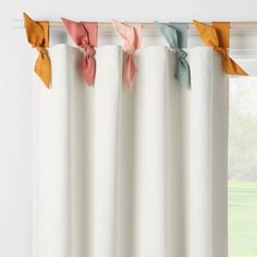 four different colored bows hanging from the top of a window curtain in front of a window