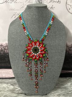 a beaded necklace with flowers and beads on a mannequin head stand in front of a wall