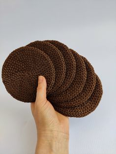 a hand holding four brown knitted coasters