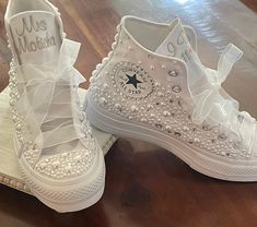 two pairs of white shoes with pearls and bows on the bottom one has a name written on it