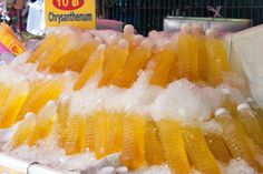 many plastic bottles filled with yellow liquid on top of ice covered trays at a market