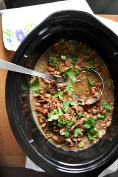 a black crock pot filled with beans and cilantro on top of a wooden table