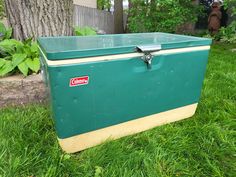 an old green and yellow cooler sitting on the grass in front of a tree,