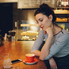 a woman sitting at a table with a cup of coffee and cell phone in front of her