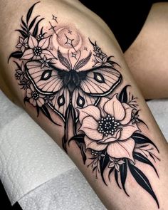 a woman's thigh with black and white tattoos on her legs, the butterfly is surrounded by flowers