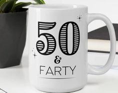 a white coffee mug with the words 50 and forty on it next to a potted plant