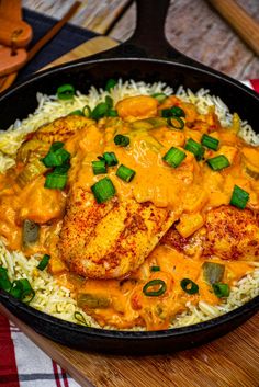 a skillet filled with rice and chicken covered in sauce on top of a wooden cutting board