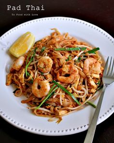 pad thai noodles with shrimp and scallops on a white plate next to a lemon wedge