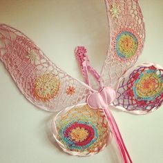 two crocheted doily angel wings and a pink ribbon on a white surface