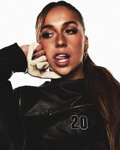 a woman with long hair wearing a black leather jacket and white gloves is posing for the camera