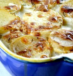 a casserole dish with potatoes and cheese in a blue bowl on a table