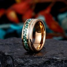 a gold ring with green and white marble inlays sits on top of a rock