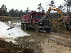 two dump trucks are parked in the mud