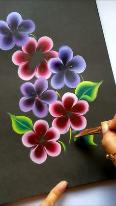 someone is drawing flowers with colored pencils on a piece of paper that they are holding in their hands