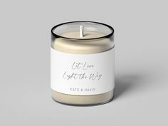 a candle with a white label on it that says let love light the way and sits in front of a gray background