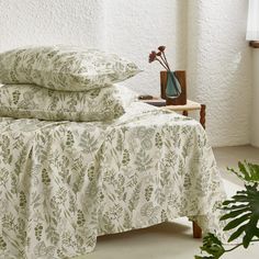 a bed with two pillows on top of it next to a potted plant in front of a window