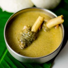 a small metal bowl filled with food on top of a green leaf