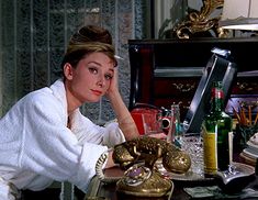 a woman sitting at a table in front of an old fashioned phone and other items