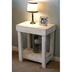 a small white table with a lamp on top and pictures on the shelf next to it