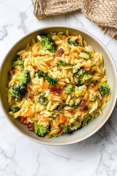 a bowl filled with pasta and broccoli on top of a marble countertop