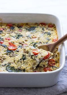 a casserole dish with spinach, tomatoes and cheese in it is being lifted by a wooden spoon