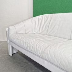 a white leather couch sitting in front of a green wall with the back end up