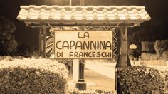 an old photo of a sign in front of some bushes and trees with the words la capannnna di francesschi written on it