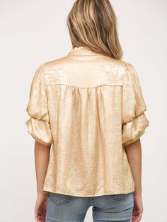 This blouse features a stunning foiled woven fabric that shimmers with elegance. Its voluminous, short-tiered sleeves add a touch of drama, while the ruffled neckline keeps the look chic and sophisticated. Perfect for evening events or holiday celebrations, this blouse is designed to make a statement. The lustrous gold fabric gives it a festive feel, making it an eye-catching piece for special occasions. SIZE & FIT Loose fit. Model is in size small. FABRIC 100% Polyester Spring Party Puff Sleeve Top With Bishop Sleeves, Spring Glamorous Shiny Blouse, Glamorous Shiny Blouse For Spring, Chic Puff Sleeve Top With Bishop Sleeves For Party, Ruffle Sleeve Blouse With Ruffles For Parties, Party Blouse With Ruffle Sleeves, Chic Shiny Blouse For Party, Glamorous Shiny Gold Tops, Elegant Puff Sleeve Top With Ruffles