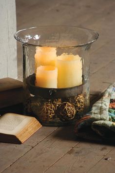 three lit candles in a glass container on top of a table next to an open book