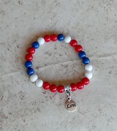 Show your Cuban pride with this beautiful Cuba flag inspired bracelet in blue, red and white colors accentuated by a small love charm in the middle. This stretchy women handmade bracelet is pre-made and ready to ship. Bracelet measures roughly 7.5" and is made with a double strand elastic cord for durability and strength.  Care For best results, keep the bracelet out of water and chemicals. Care instructions would be included in packaging.    Measurement Size 7.5 inches  Materials Antique Tibetan charm and tube bead 8 MM Glass beads Stretch elastic Patriotic White Stretch Bracelet With Round Beads, Patriotic White Stretch Bracelet, Patriotic Red Beaded Bracelets As Gift, Patriotic Red Friendship Bracelet As Gift, Patriotic Blue Friendship Bracelets As Gift, White Patriotic Bracelet As Gift, Patriotic White Friendship Bracelets As Gift, Patriotic White Stretch Bracelet As Gift, Patriotic White Friendship Bracelets Gift