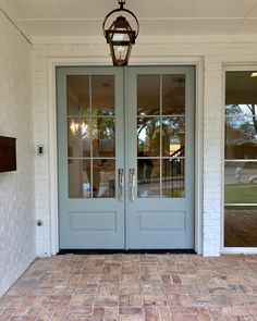 the front door to a home with two glass doors and brick walkway leading into it