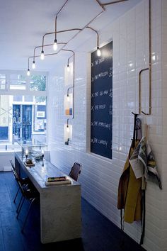 a long table in a room with white tile walls and wooden floors, along with hanging lights