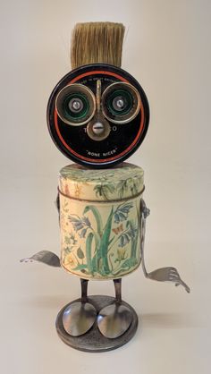 an odd looking object with two eyes and a brush in it's head, sitting on top of a tin can