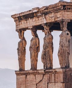 some statues on the side of a building with mountains in the backgrouds