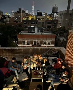 group of people sitting on top of a roof with city lights in the back ground