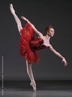 the ballerina is dressed in red and has her arms stretched out while she stands on one leg