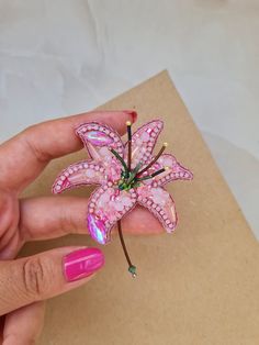 a woman's hand holding a pink flower brooch on top of a piece of paper