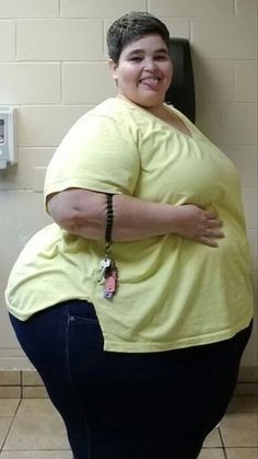 a woman standing in front of a urinal with her arms over her stomach and smiling