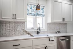 a kitchen with white cabinets and blue patterned blind shades on the window sill above the dishwasher