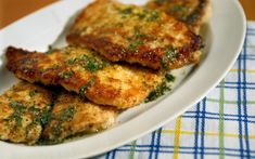 two pieces of chicken on a white plate with parsley and seasoning over the top