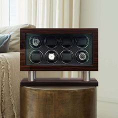 a watch winder sitting on top of a table in front of a couch and window