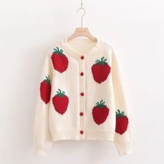 a white sweater with strawberries on it hanging from a hanger against a wall