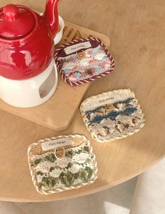 three coasters sitting on top of a wooden table next to a red teapot