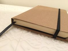 a book with a black ribbon is sitting on a white tablecloth and has a brown cover