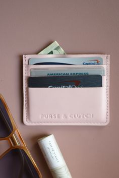 an american express credit card holder next to sunglasses and money on a pink surface with gold rimmed glasses