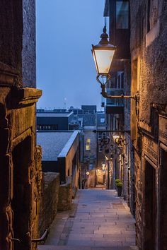 an alley way with stone buildings and street lamps on either side, at night time