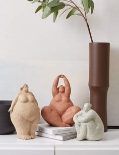 three ceramic sculptures sitting on top of a white table next to a vase with a plant in it