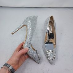 a person is holding two pairs of silver high heeled shoes with crystals on them