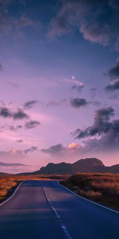 an empty road in the middle of nowhere at dusk, with mountains in the distance